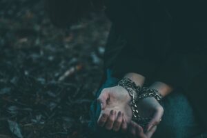 Close-up of a person's hands bound with chains in an outdoor setting, symbolizing confinement.
