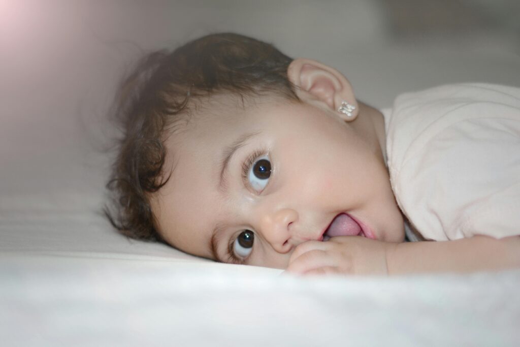 Charming baby girl with big brown eyes lying on bed, showing innocence and cuteness.