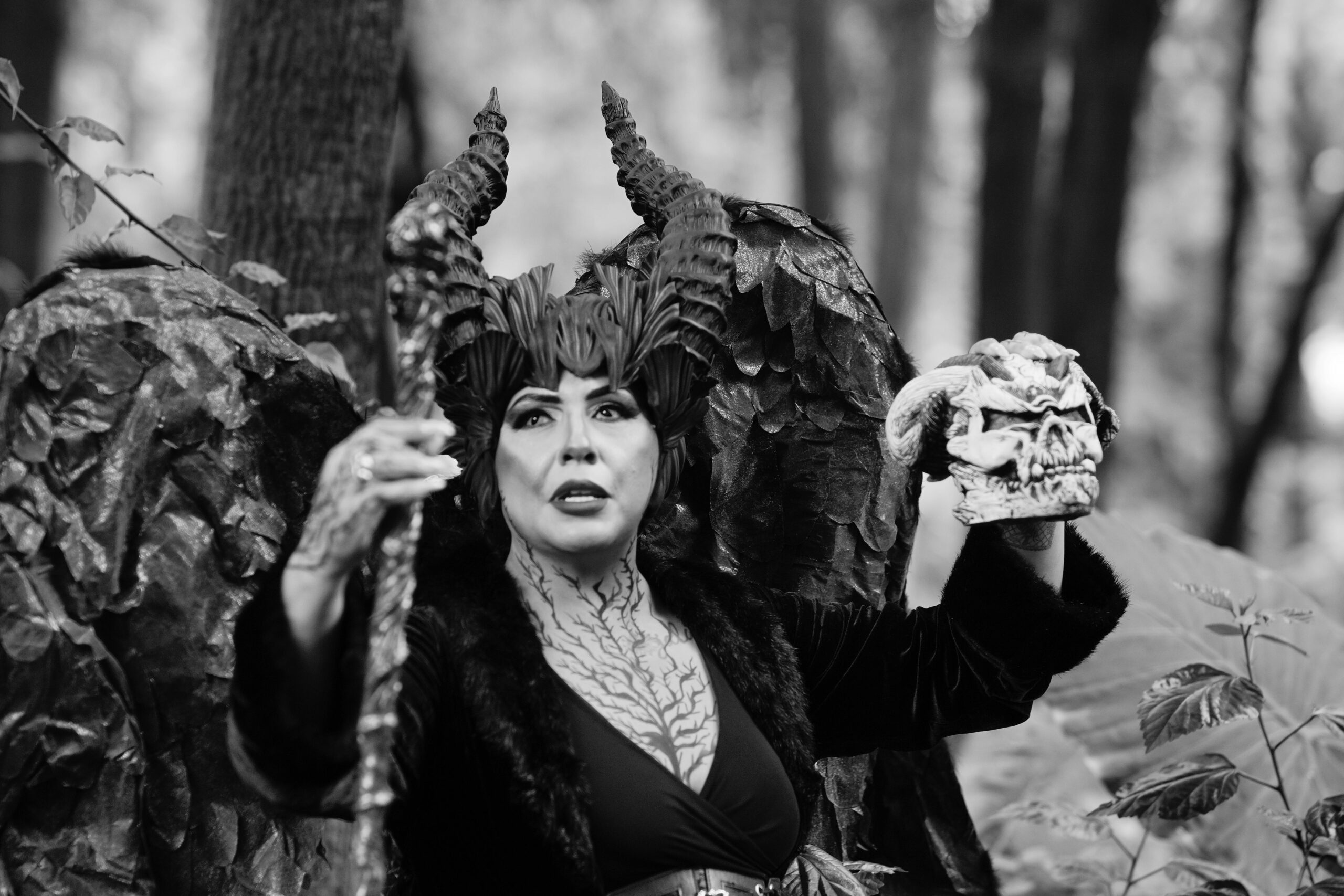 Dramatic portrait of a sorceress with horns in a forest, holding a skull.