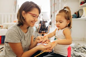 Mother and daughter bonding over arts and crafts at home, painting playful heart designs.