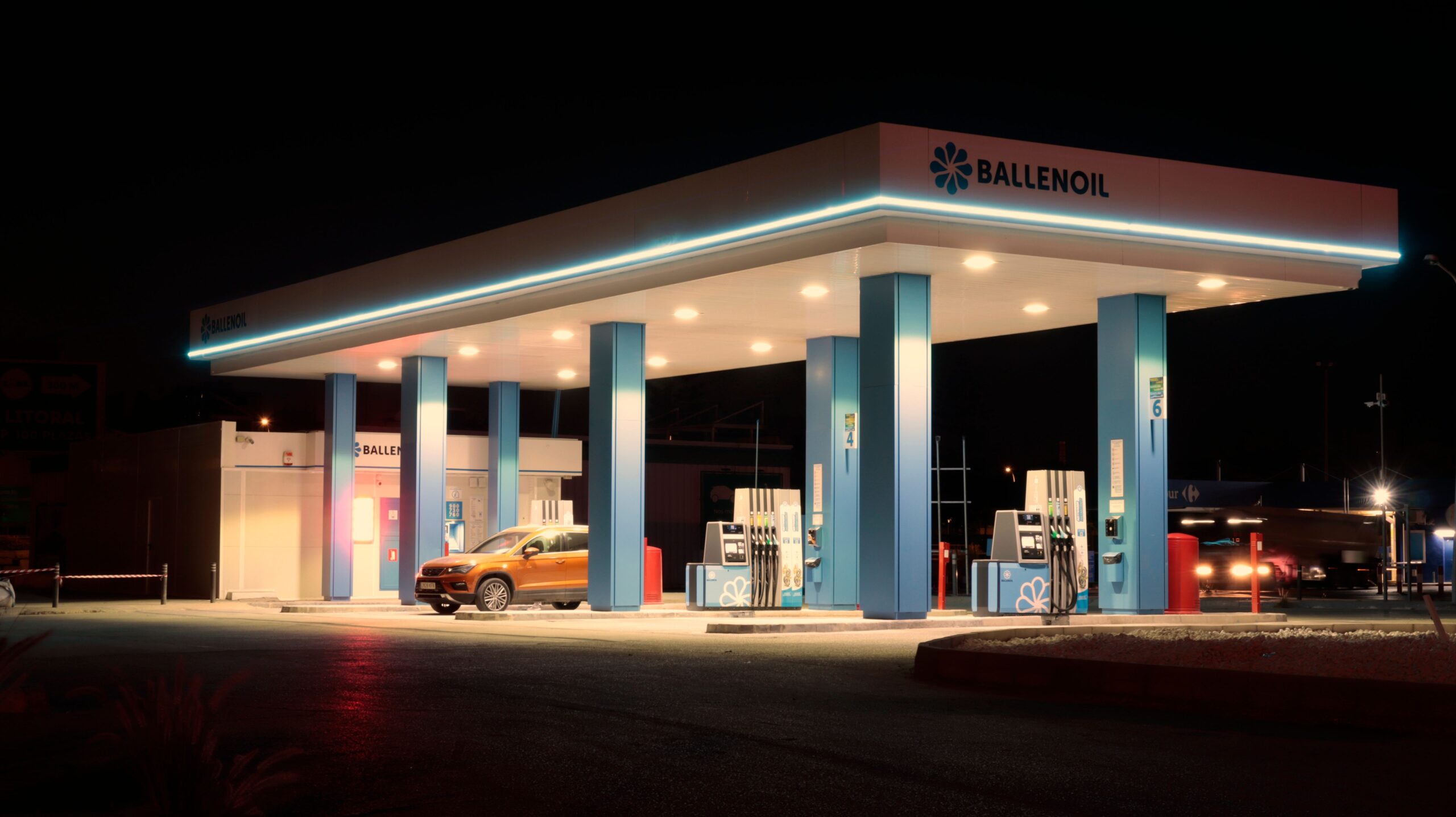 Brightly lit Ballenoil gas station in Málaga, captured during night with warm lighting.